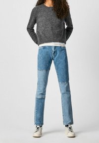 Gray textured sweater, layered over a white shirt, paired with blue patchwork jeans and white sneakers. Simple and modern design.