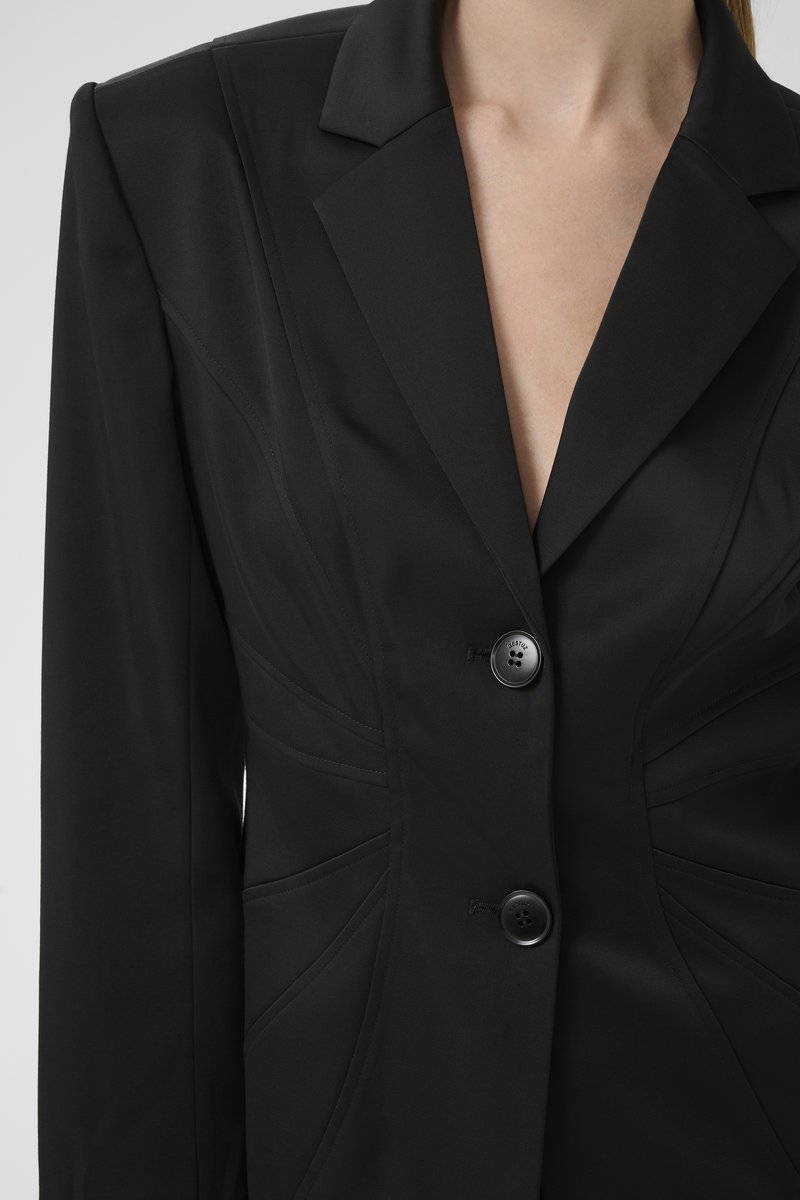 Black tailored blazer featuring a notched lapel, two large buttons, curved seam details, and a sleek, smooth texture.