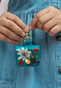 Turquoise leren sleutelhangerhouder met bloemmotief, gouden hardware, drukknoopsluiting en decoratieve accenten in rood en groen.