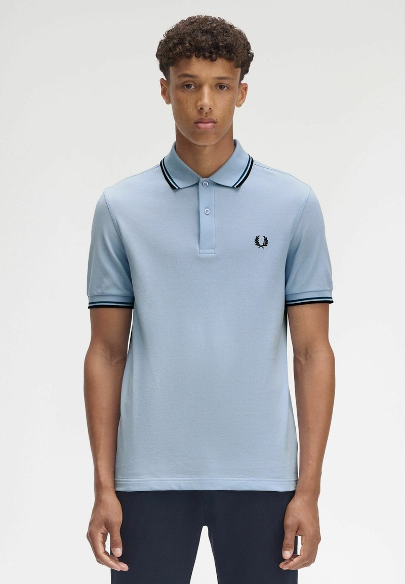 Hellblaues Poloshirt aus weichem Stoff, mit einem schwarz gestreiften Kragen und Bündchen, drei Knöpfen und einem kleinen gestickten Logo auf der Brust.