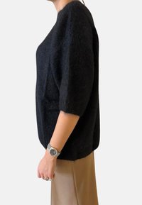 Maglione nero in maglia strutturata con una vestibilità ampia, scollo rotondo e maniche a tre quarti, abbinato a una gonna beige. Orologio argento al polso.