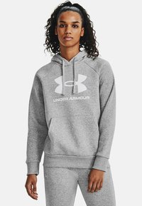 Szara bluza z kapturem wykonana z miękkiego materiału, z dużym białym logo Under Armour oraz kieszenią z przodu. Rękawy raglanowe i ściągacze. 