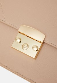 Zbliżenie na beżową, teksturowaną skórę z prostokątną złotą metalową klamrą z dwoma okrągłymi guzikami i centralnym okrągłym detalem.