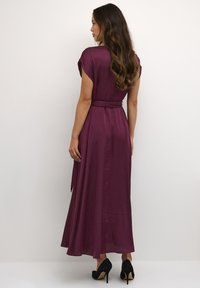 Langes burgunderfarbenes Kleid mit kurzen Ärmeln, tailliertem Bund und fließendem Rock, kombiniert mit schwarzen High-Heels. Glatte Textur und leichtes Material.
