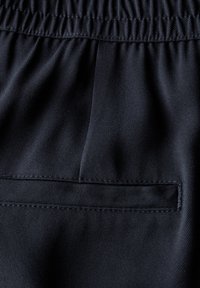Mørkeblå stof med en struktureret overflade. Har en elastisk talje og en enkelt lomme med et skjult design.