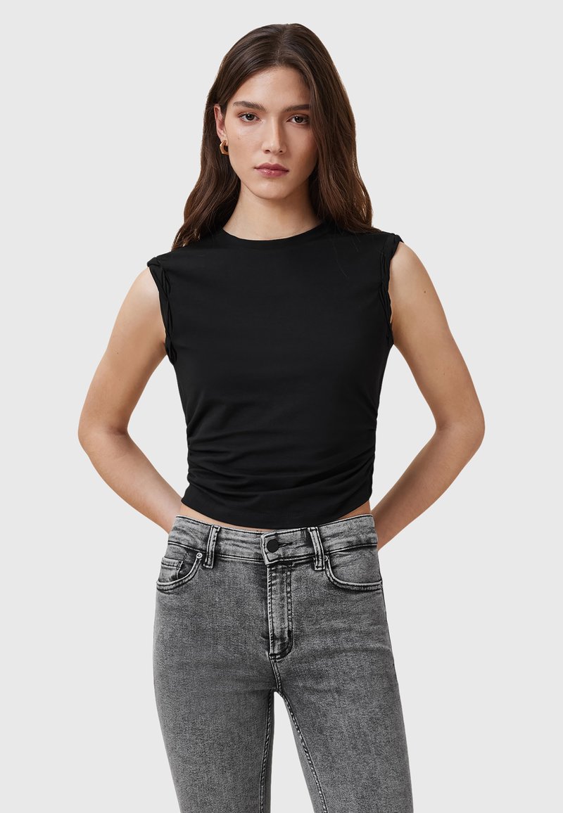 Top nero senza maniche con texture arricciata in vita, abbinato a jeans grigi a vita alta con un classico design a cinque tasche.