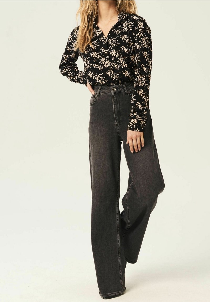 Blusa nera floreale abbinata a jeans scuri in denim a vita alta e dal taglio morbido. La blusa presenta un colletto e maniche lunghe con chiusure a bottoni.