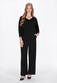 Zwarte trui met glinsterende accenten, V-hals ontwerp, gecombineerd met hoge zwarte broeken en zwarte hoge hakken. Elegante en stijlvolle uitstraling.
