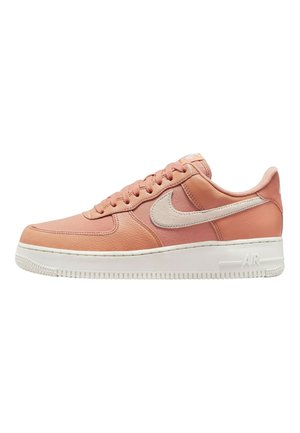 Zapatillas Nike Air Force 1 de color rosa claro con parte superior de cuero, cuello acolchado y suela de goma blanca. Logo signature en un beige contrastante.