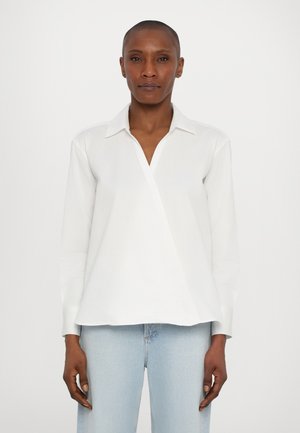 Witte langslijfsblouse met een lichte wikkeldesign, puntige kraag en een gladde textuur. Gecombineerd met lichtblauwe denim broek.
