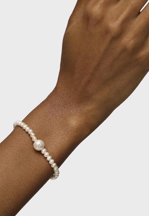 Pulsera de perlas con perlas blancas irregulares y una única perla central más grande, ensartada en un hilo flexible y texturizado.