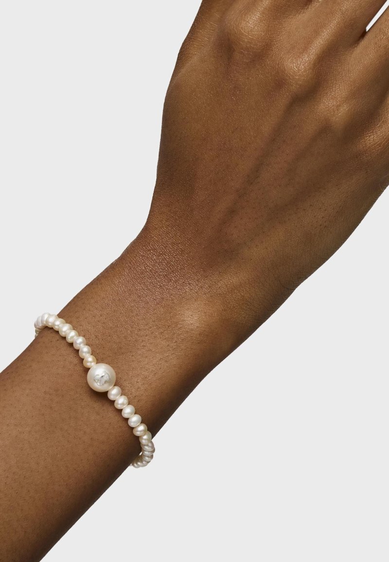 Pulsera de perlas con perlas blancas irregulares y una única perla central más grande, ensartada en un hilo flexible y texturizado.
