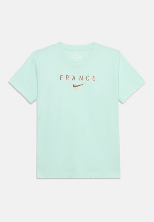 T-shirt bleu clair à manches courtes avec col rond, arborant le mot "FRANCE" et un logo Nike en forme de swoosh marron au centre de la poitrine.