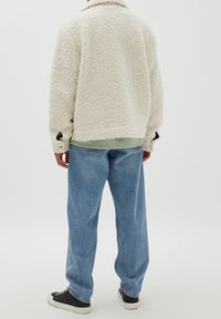 Cremefarvet fleecejakke med en tekstureret overflade, der har krave og sorte accenter, parret med lyseblå denimbukser.