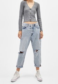 Grå ribbad långärmad cardigan med knappstängning, i kombination med ljusblå slitna jeans och vita sneakers.