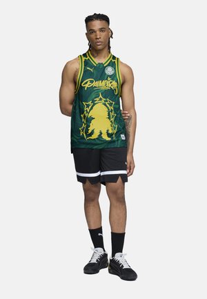 Grön nät-baskettröja med gul design och bokstäver, ihop med svarta shorts med vita accentstrimmor. Svarta sneakers fulländar looken.
