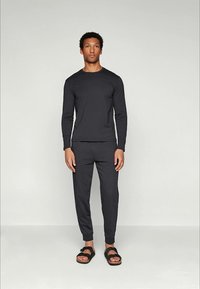 Haut noir à manches longues et pantalon fuselé en tissu doux, associés à des sandales noires ; design simple sans motifs ni accents visibles.