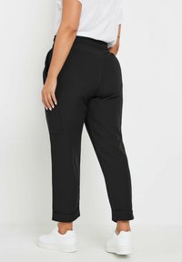 Pantalones negros ajustados con una textura suave, con puños enrollados y bolsillos laterales, combinados con zapatillas blancas. Detalle de costura visible en los bolsillos.