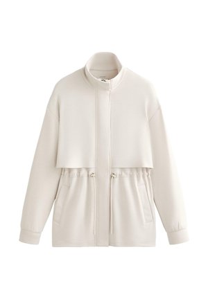 Licht beige jas met ritssluiting, hoge kraag, taille koord en twee voorzakken. Gemaakt van zachte, gestructureerde stof met een ontspannen pasvorm.