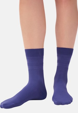 Gambe con calzini viola a coste fino a metà polpaccio, con due sottili strisce orizzontali vicino alla parte superiore, mostrati su uno sfondo semplice.