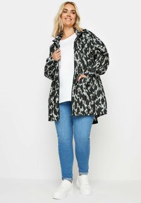 Svart- och vitmönstrad vattentät jacka med dragkedja, lös passform och sidofickor, bärs över en vit topp och blå jeans, ihop med vita sneakers.