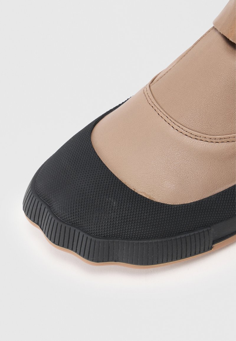Beige and black slip-on shoe with textured rubber front; smooth leather upper; rounded toe; contrasting materials and colors.