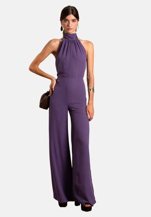 Paars halter jumpsuit met geplooide halslijn en een wijdere pijpdesign, gemaakt van een gladde stof. Accessoire: kleine bruine handtas.