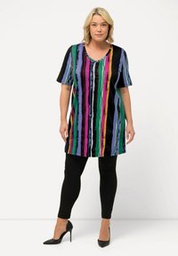 Túnica multicolor con rayas verticales en púrpura, verde, rosa y negro, escote en v, mangas cortas, combinada con leggings negros y tacones.