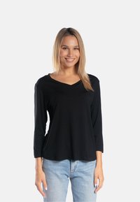 Czarna bluzka z długim rękawem w dekolcie V, uszyta z miękkiego materiału, lekko luźny krój, w zestawie z jasnoniebieskimi dżinsami.