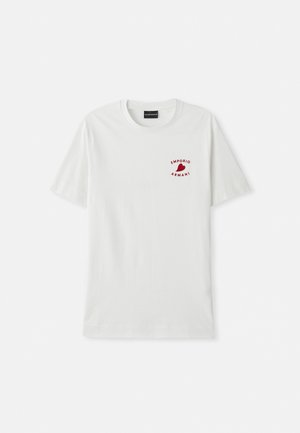 T-shirt en coton blanc à manches courtes et col rond. Présente un logo rouge sur la partie gauche de la poitrine. Texture lisse, coupe décontractée.