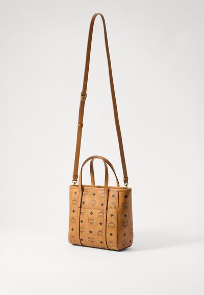Tan leather small tote bag with repeated black MCM logo pattern, two short handles, and one long adjustable shoulder strap.
