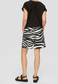 Haut noir à manches courtes associé à un short zèbre noir et blanc. Les sandales présentent un design de bride tissée et une semelle épaisse.