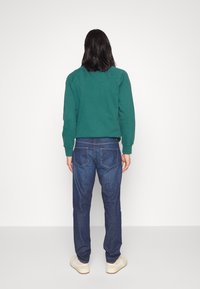 Grön crewneck sweatshirt med ribbad muddar, parat med blå denimjeans med klassisk femficksdesign och synlig sömnad.