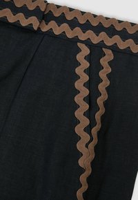 Mustast kangast rõivas, millel on pruunid lainelised ääred vööjoonel ja vertikaalsete õmbluste detailid, rõhutades tekstureeritud dekoratiivset õmblust.