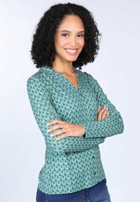 Grüne Bluse mit langen Ärmeln und V-Ausschnitt, mit einem wiederkehrenden blauen und lila Muster, schlanker Schnitt und weicher Textur. Knopfverschluss vorne.