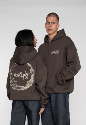 Felpa marrone con zip frontale, con un logo sul petto e un grande design grafico circolare sul retro. Realizzata in tessuto morbido.