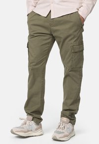Pantalones cargo verde oliva con múltiples bolsillos laterales, material de algodón, corte recto y costuras decorativas, combinados con zapatillas ligeras.