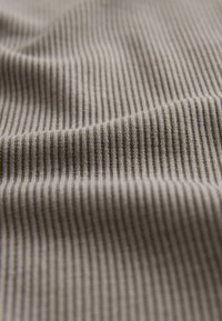 Textil i en ljusbrun ton med en fin ribbad struktur, som visar subtila veck och veck, vilket framhäver dess materialstruktur.