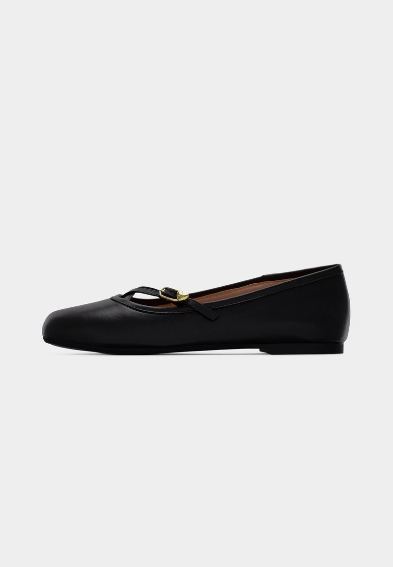 Chaussure plate en cuir noir avec une fine bride et une petite boucle dorée en forme de cœur, bout arrondi et petit talon.