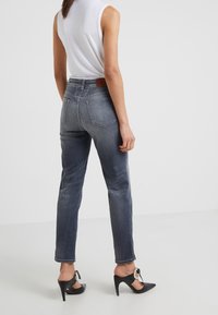 Jeans de mezclilla en gris oscuro con corte recto y bolsillos traseros. Llevados con una blusa sin mangas blanca y zapatos de tacón alto negros.