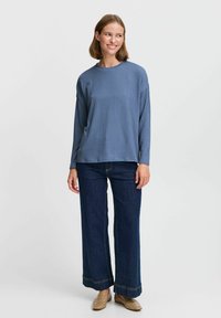 Löst sittande, ribbad långärmad topp i mjuk blå färg, tillsammans med högmidjade, vida mörkblå jeans med kontrasterande sömmar och beigea sko-slip-ons.