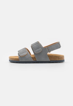 Grå ruskind sandal med to justerbare stropper over foden og en omkring hælen, korkfodbed og sort gummisål.
