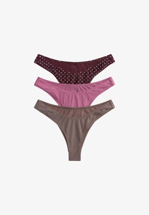 Young woman with short dark hair wearing a maroon polka dot strapless bikini standing against a plain light background.