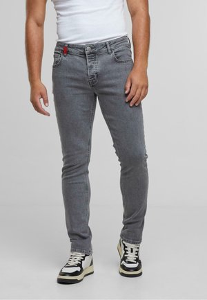 Grijze skinny jeans van denim met een vijf-pocket ontwerp en een rode accentlus bij de tailleband, gecombineerd met zwart-witte hoge sneakers.