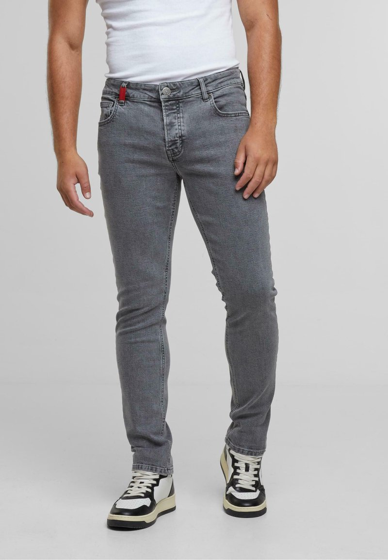 Jeans skinny de mezclilla gris con un diseño de cinco bolsillos y un lazo rojo en la cintura, combinados con zapatillas altas negras y blancas.