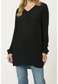 Haut noir à manches longues avec un col en V, présentant un tissu texturé et une coupe décontractée, associé à un denim bleu clair.