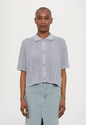 Light gray textured knit short-sleeve shirt with a collar and button front. Worn over a denim skirt with a slit.