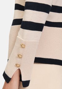 Gestreepte gebreide trui in lichtbeige en marineblauw, met een geribbelde textuur en drie gouden knoopaccenten bij de manchetten. Heeft een gespleten zoom.