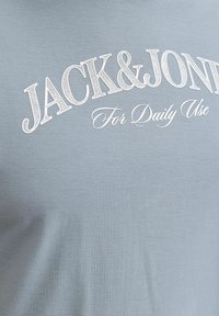 Tissu bleu clair avec texte blanc "JACK & JONES" en grandes lettres et "For Daily Use" en plus petit en écriture cursive en dessous.