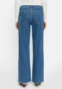 Široke plave traperice s visokim strukom, koje imaju dvije stražnje džepove i klasičan završetak. Tkanina izgleda čvrsto s laganom teksturom.